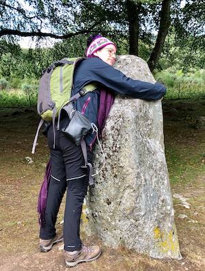 A woman in hiking clothing hugging a standing stone illustrating a post about presence